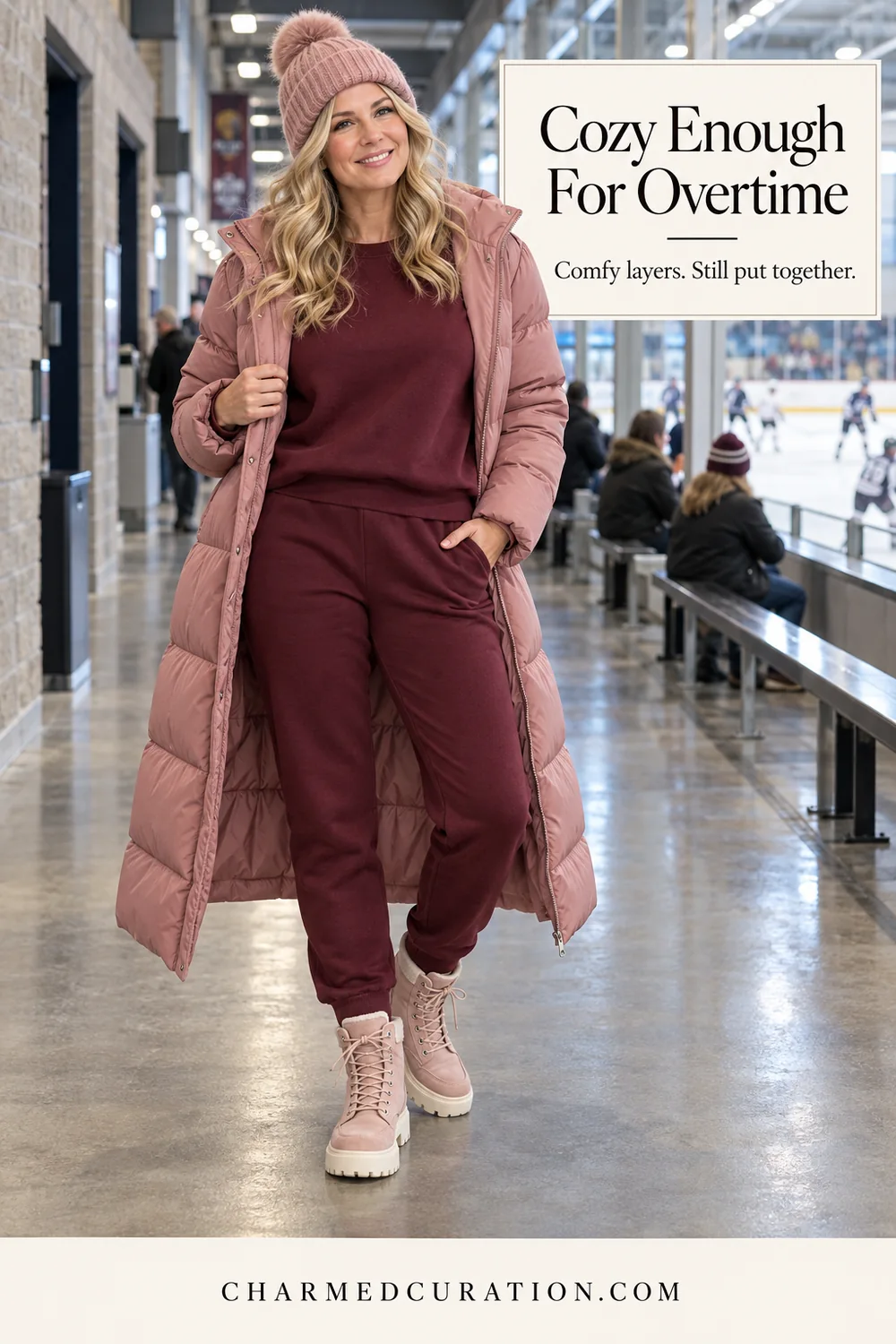 Woman beside a hockey rink wearing burgundy matching sweats, a long rose puffer, a pink knit hat and pink lace-up boots.